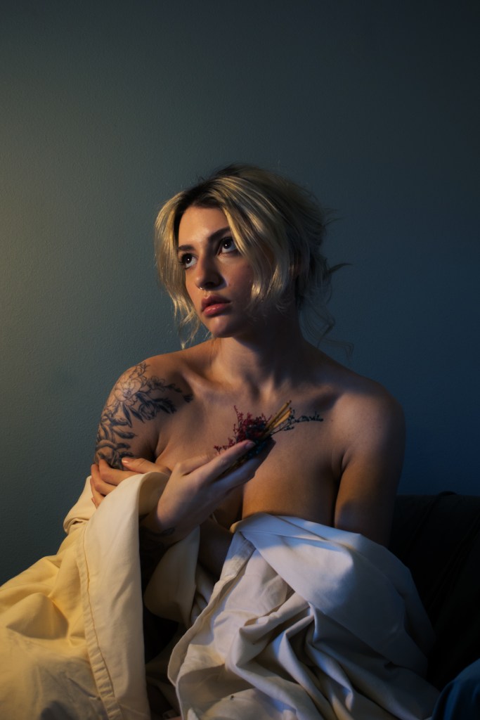 Portrait in Renaissance style of a blonde woman draped in fabric, holding a small floral bundle 